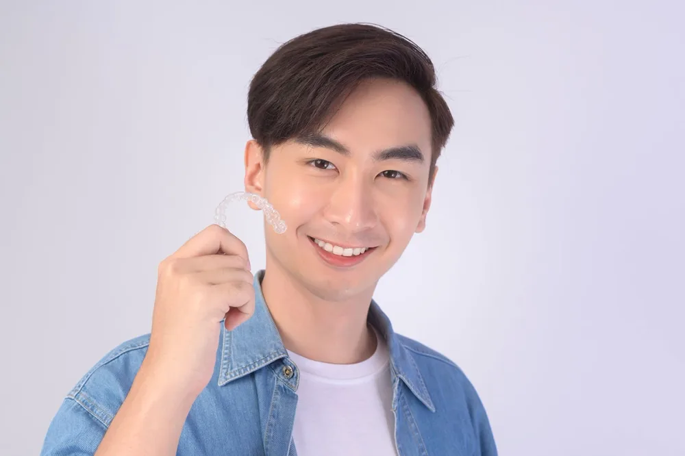 A smiling patient holding a clear aligner